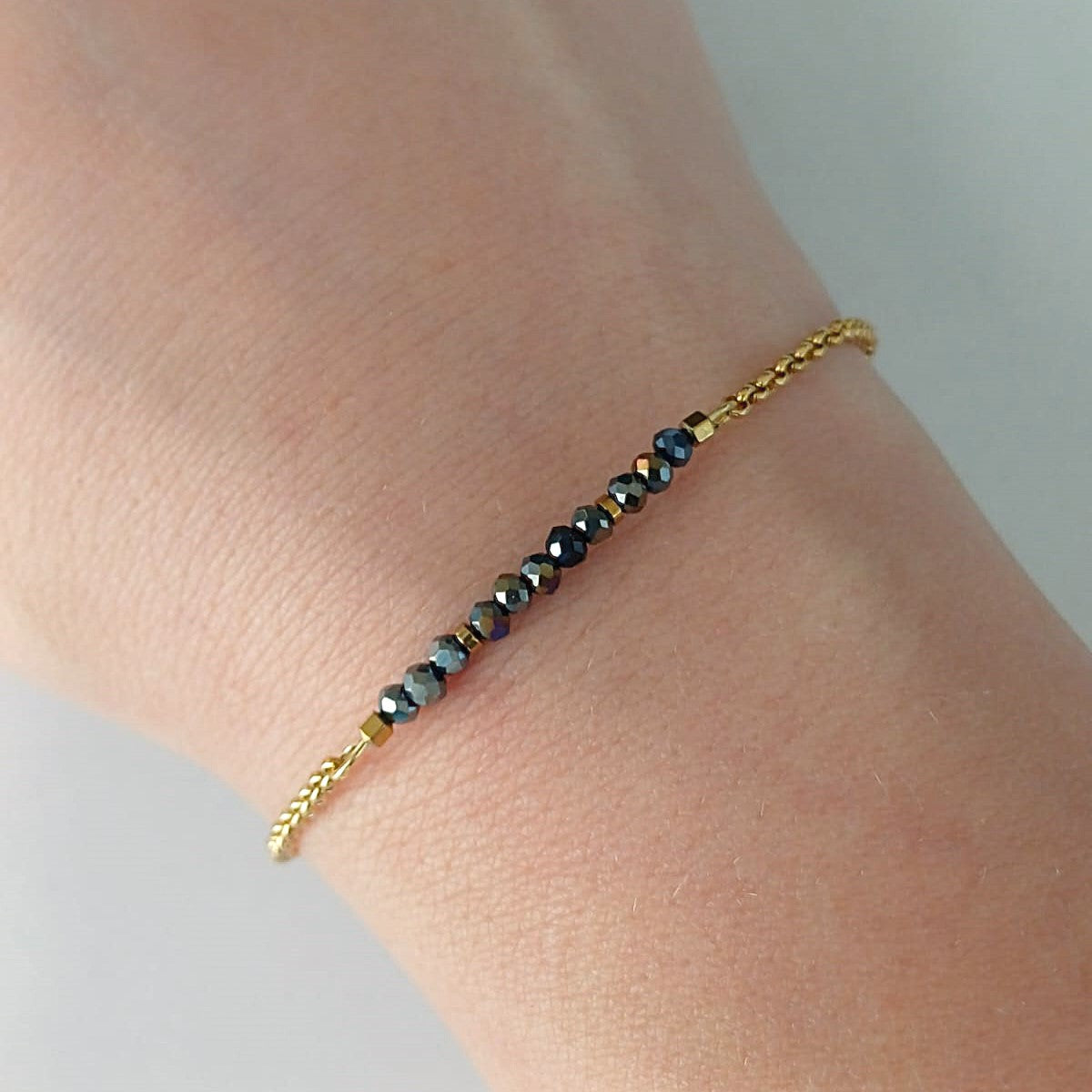 Goudkleurige RVS armband met zwarte facetkraaltjes met iriserende glans – elegant en verfijnd dames sieraad.