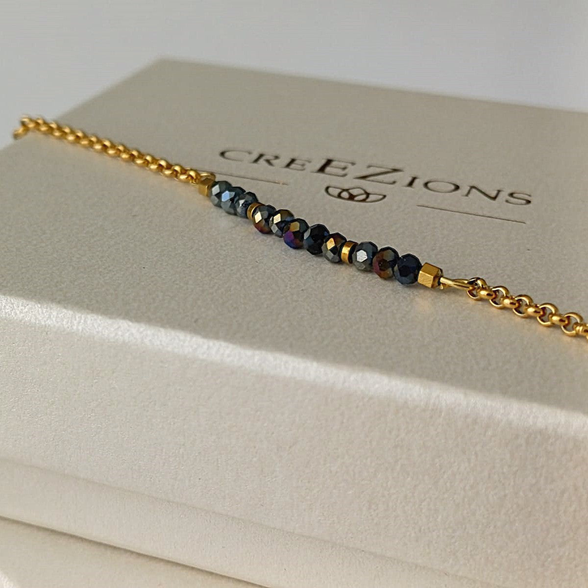 Goudkleurige RVS armband met zwarte facetkraaltjes met iriserende glans – elegant en verfijnd dames sieraad.